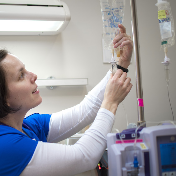 A nurse in blue scrubs adjusts an IV bag.