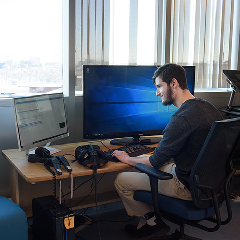 A student works at a computer with two large monitors.