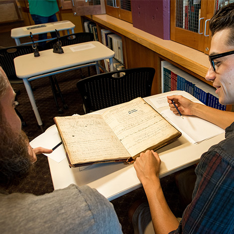 Two students review a historical book in the library.
