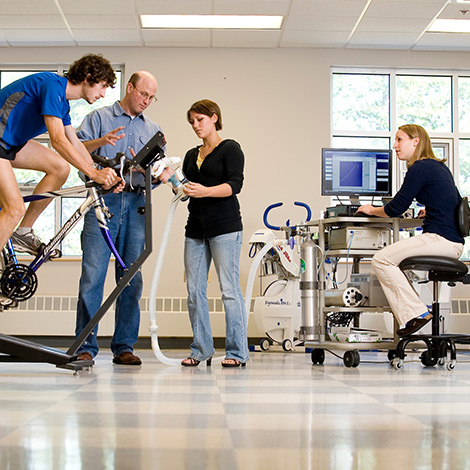 Students and faculty monitor a student on an exercise bike, in an health science lab.