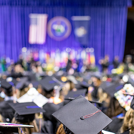 A group of graduates in their cap and gowns, facing a stage.