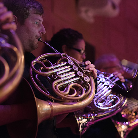 A group of french horn players perform.