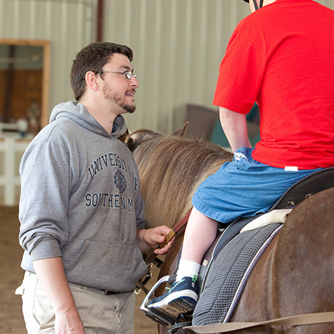 A recreational leisure student works with a client who is riding a horse as part of therapeutic recreation.