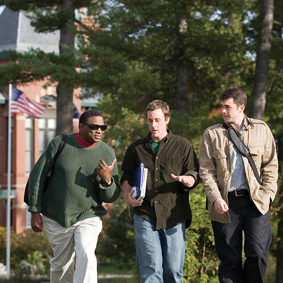 Three graduate students talk to each other while walking on the USM Gorham campus.