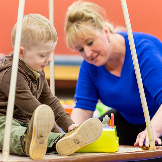 An occupational therapy faculty works with a child who sits on a swing in the OT clinic.