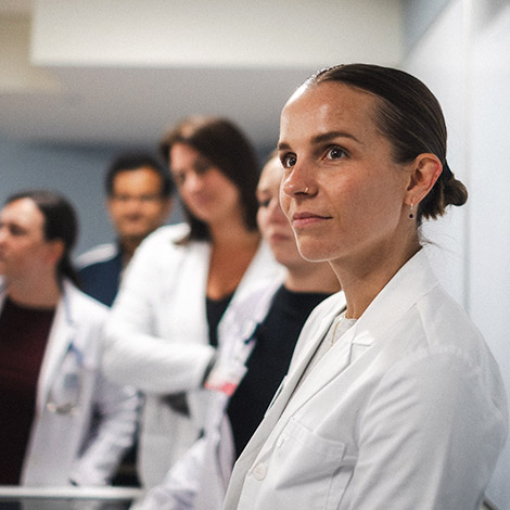 A graduate nursing student looks toward an instructor, with a groups of fellow students standing behind her.