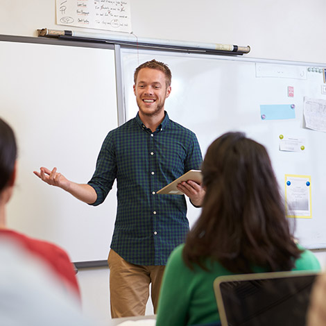 A teacher stands and talks at the front of a classroom.