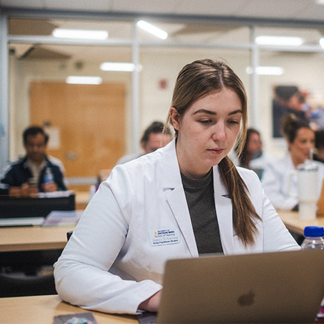 A graduate nursing student sits and types on a laptop during class.