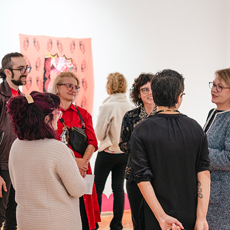 A group of students, faculty, and parents talk with each other at an art exhibition opening in the USM Art Gallery.