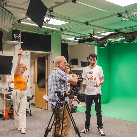 A group of students work with camera equipment in front of a green screen in a media production lab.
