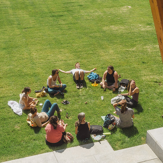 A group of students sit in a circle in the grass outside of the McGoldrick Center for Career and Student Success.