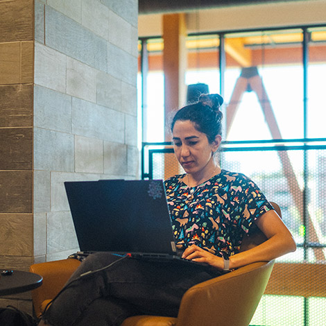A student sits and types on a laptop that is on her lap.