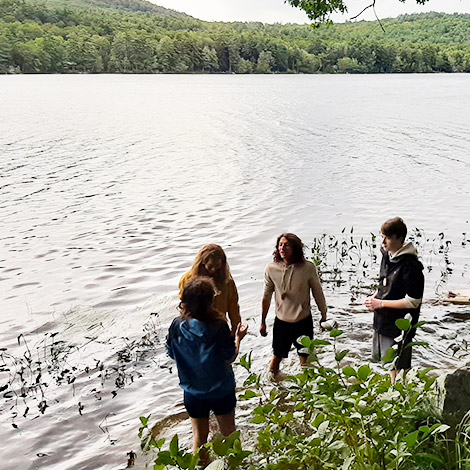 A group of students wade on the edge of a lake.