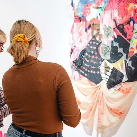 Two students view a piece at an art exhibition opening reception.