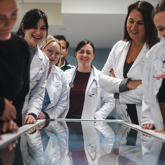 A group of graduate nursing students gather around a table in a simulation lab.