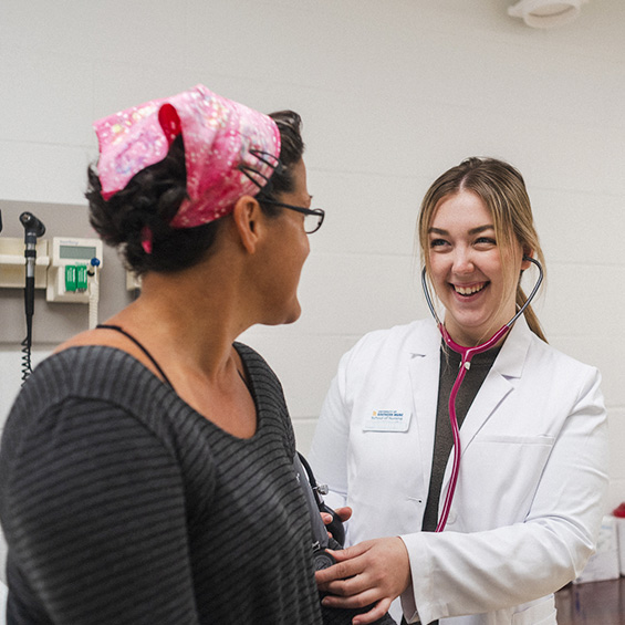 A nursing student in a lab coat smiles at a patient.