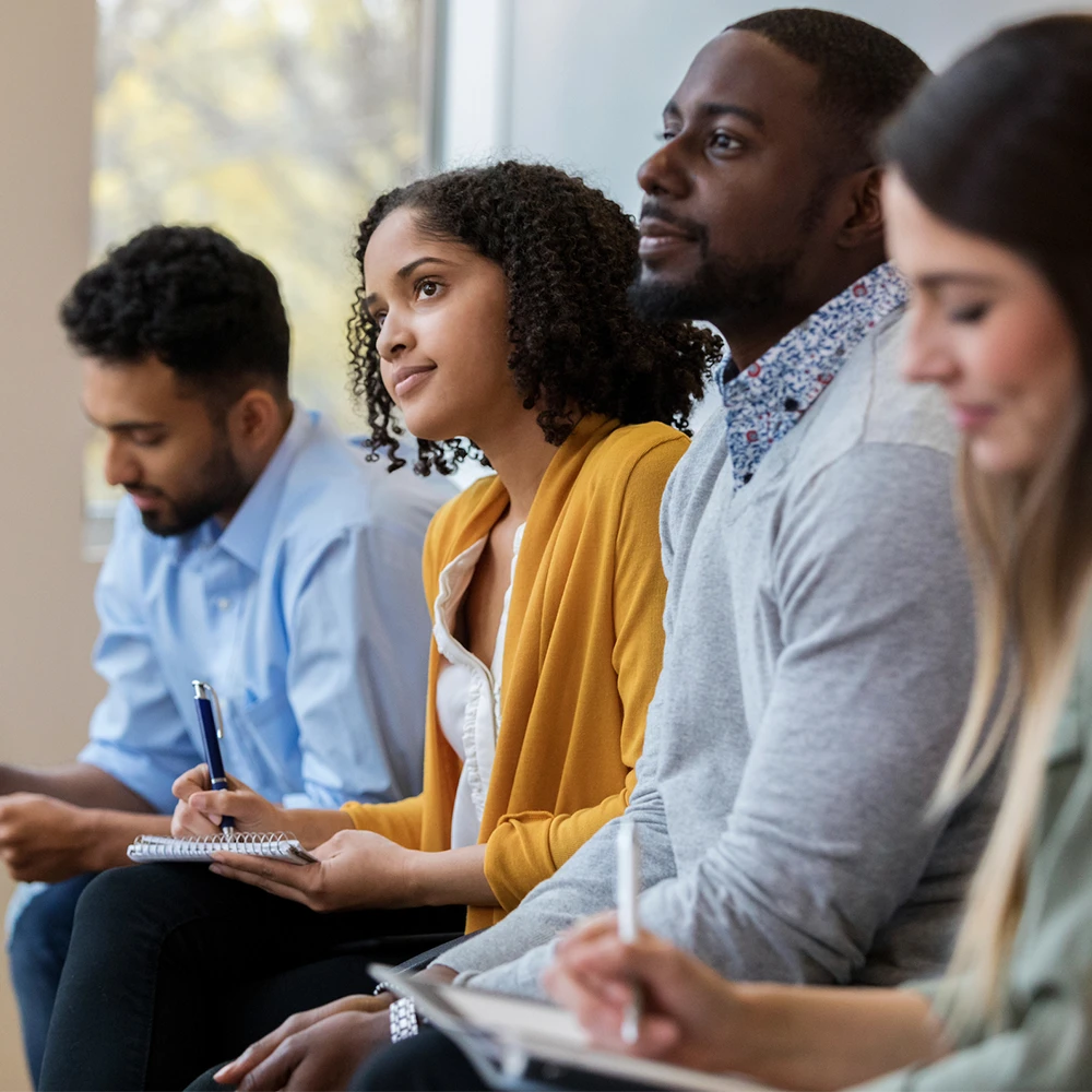 A group of four students sit and take notes, with two students looking up attentively.