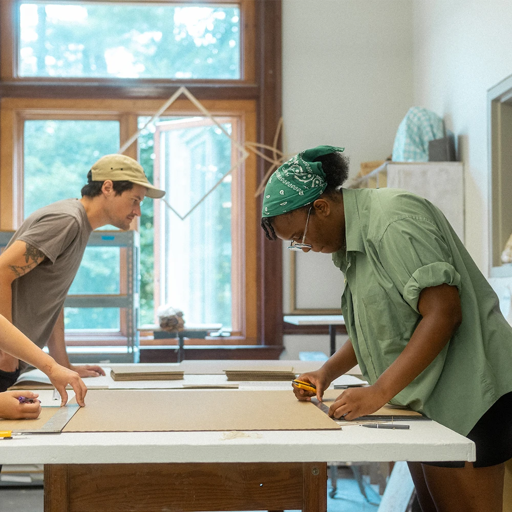 Two students lean over a table and sketch.