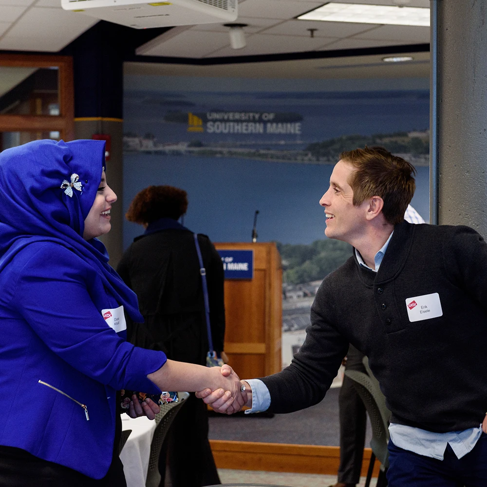 A student shakes hands with a business person at a networking event.