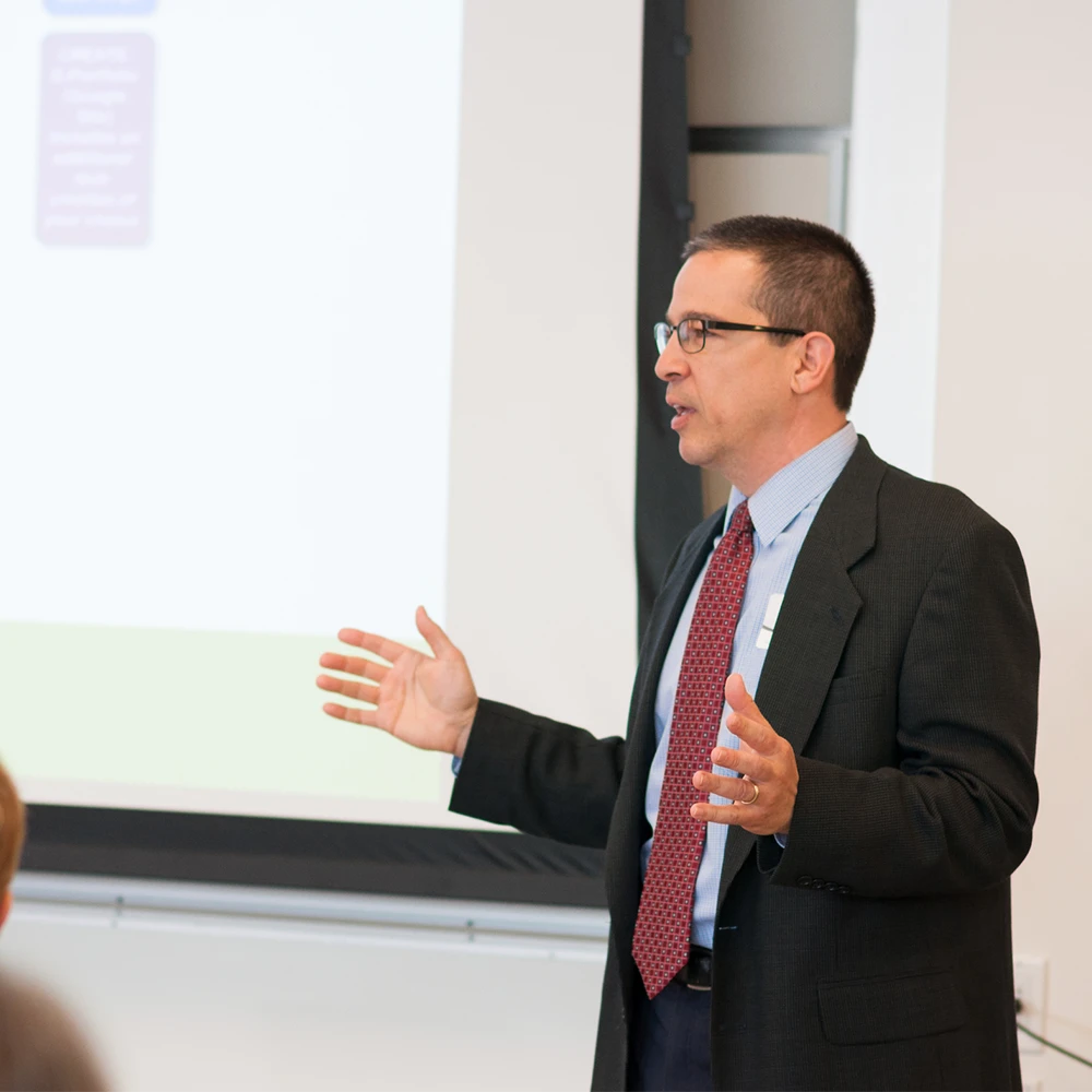 A faculty member speaks in front of a presentation screen.