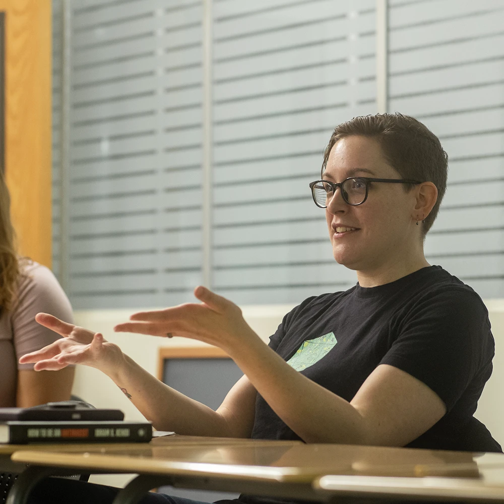 A person sits at a table and gestures with their hands while talking.