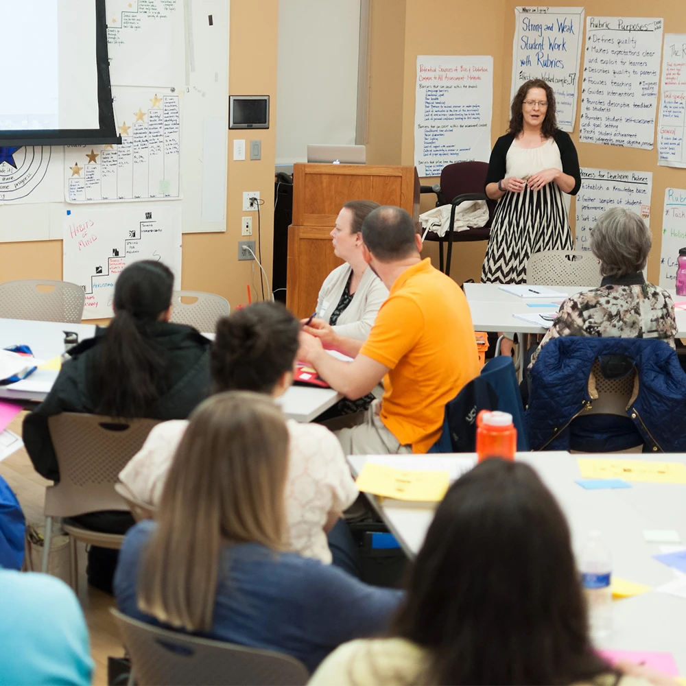 A faculty member speaks to a large crowd of adults seated at tables.