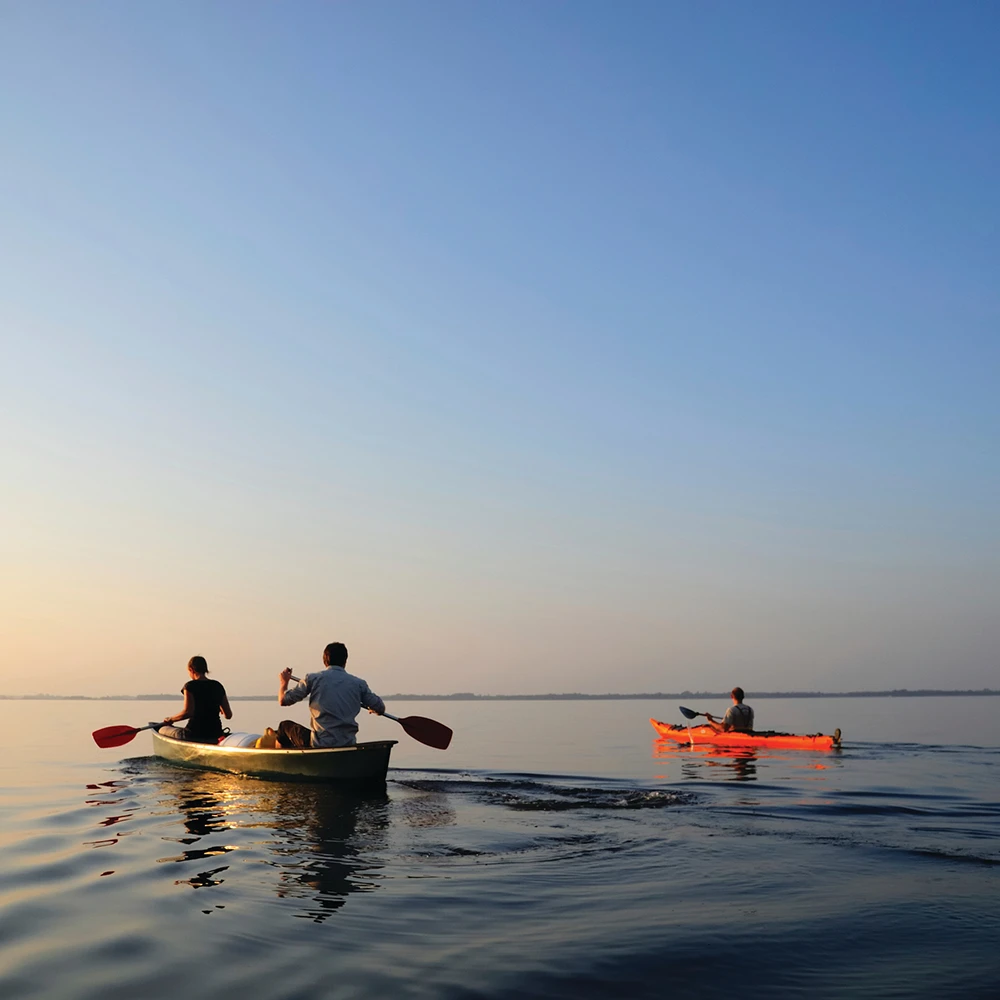 Two people in a canoe and one person in a kayak paddling on the ocean.