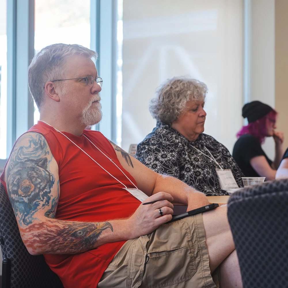 A group of three students sit at different tables and look in the same direction, listening to someone.