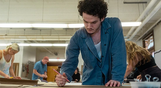 A student leans over a table and sketches.