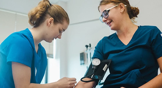 Two nursing students work together to practice using a blood pressure monitor.