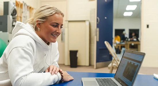 A student sits at a medical table and works on a laptop.