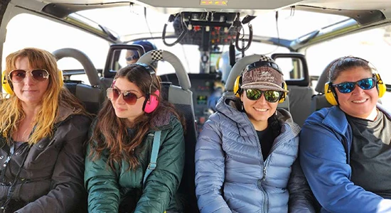 Four students ride on a helicopter, wearing sunglasses and earmuffs.