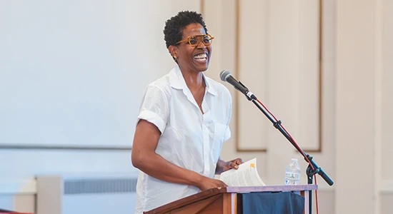 A woman stands at a podium and speaks into a microphone, with papers in front of her.