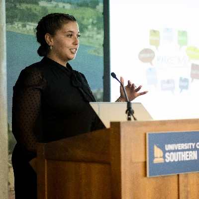 A student adjusts a microphone at a podium with the USM logo on the front.