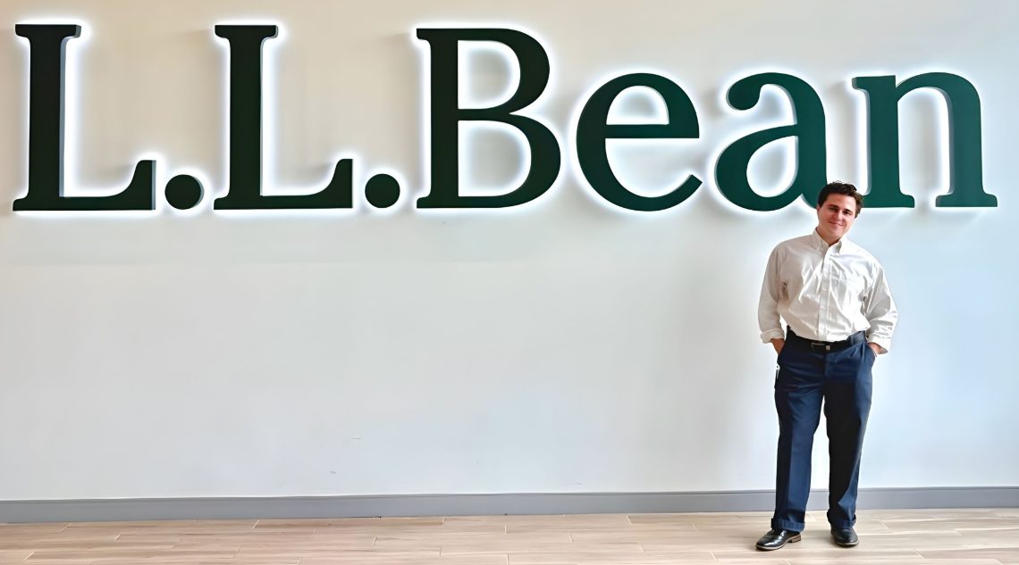 Maxfield Rhine standing in front of the L.L.Bean logo at L.L.Bean HQ in Freeport, ME
