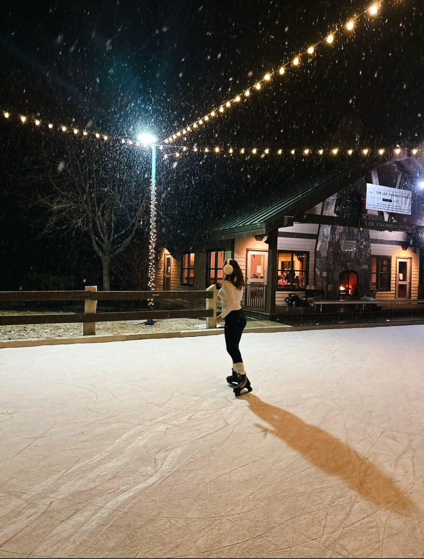 Person ice skating on the frozen Lee Twombly Pond at night surrounded by twinkling lights in Falmouth, Maine