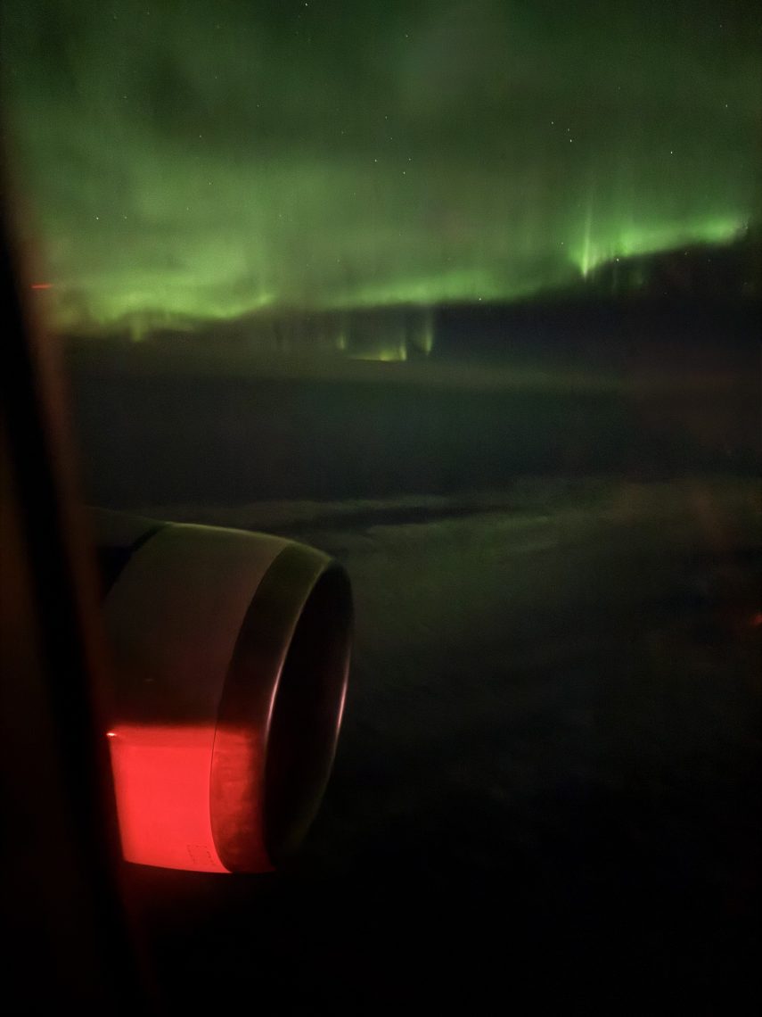 View of the northern lights over Iceland seen through an airplane window at night