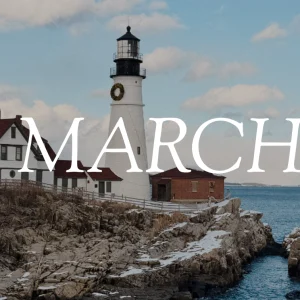Portland Head Light lighthouse is covered in snow and surrounded by snowy rocks above the ocean. The word "March" overlays the image