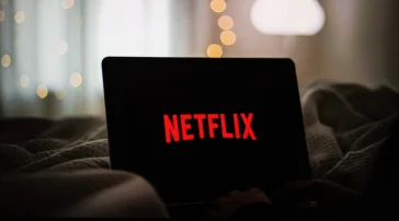 A laptop sits open on a bed with the Netflix logo lit up on its screen.