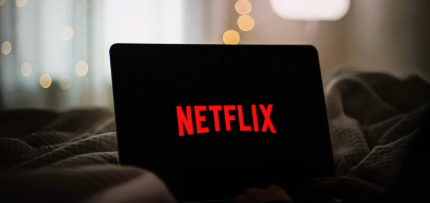 A laptop sits open on a bed with the Netflix logo lit up on its screen.