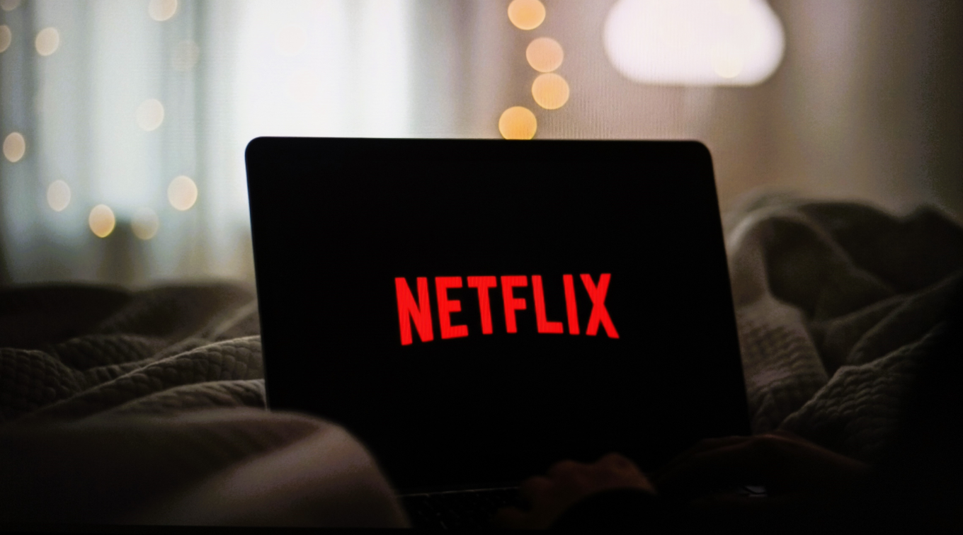 A laptop sits open on a bed with the Netflix logo lit up on its screen.