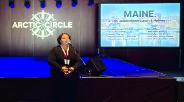 Emily Ireland delivers a speech at a microphone at the Maine luncheon during the Arctic Circle Assembly.
