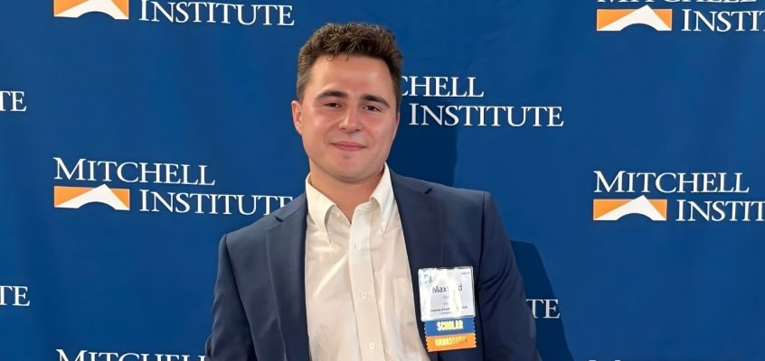 Maxfield Rhine standing in front of Mitchell Institute step and repeat.