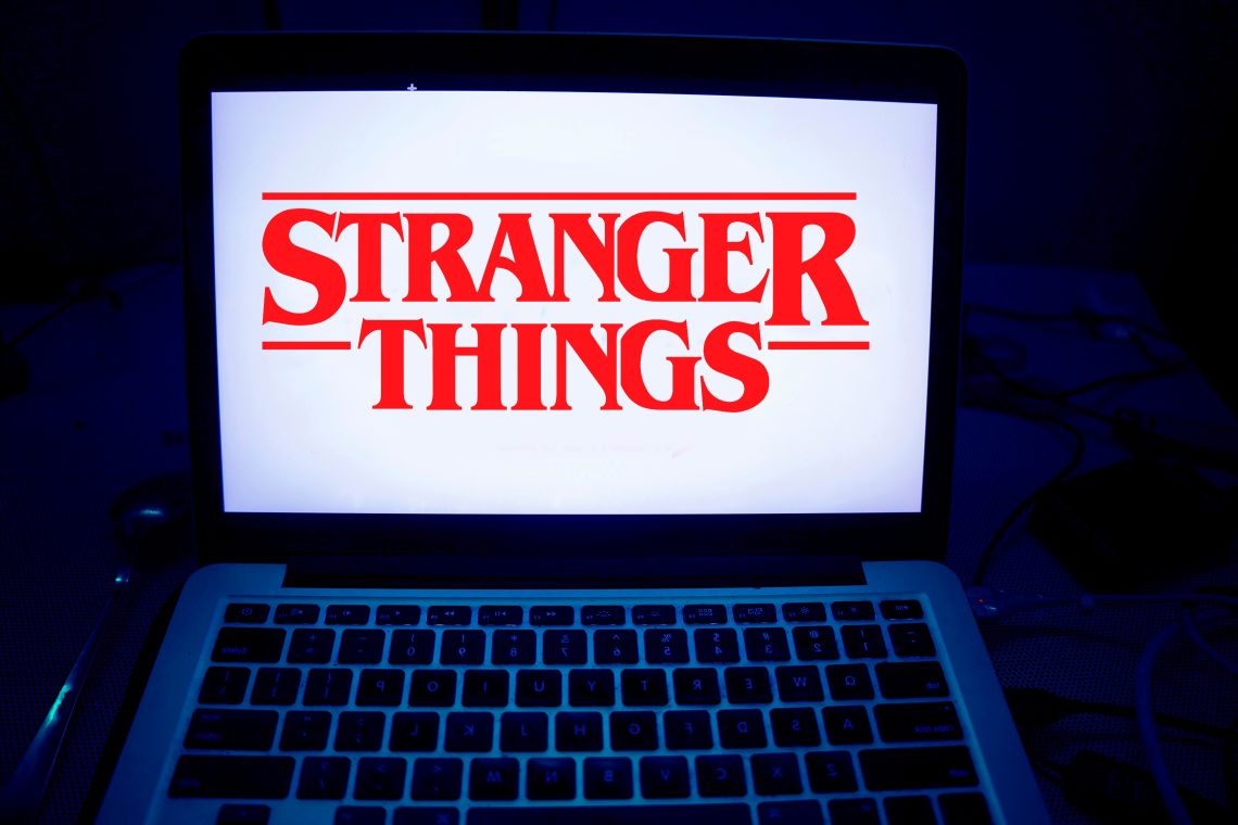 Laptop computer with Stranger Things logo lighting up screen.
