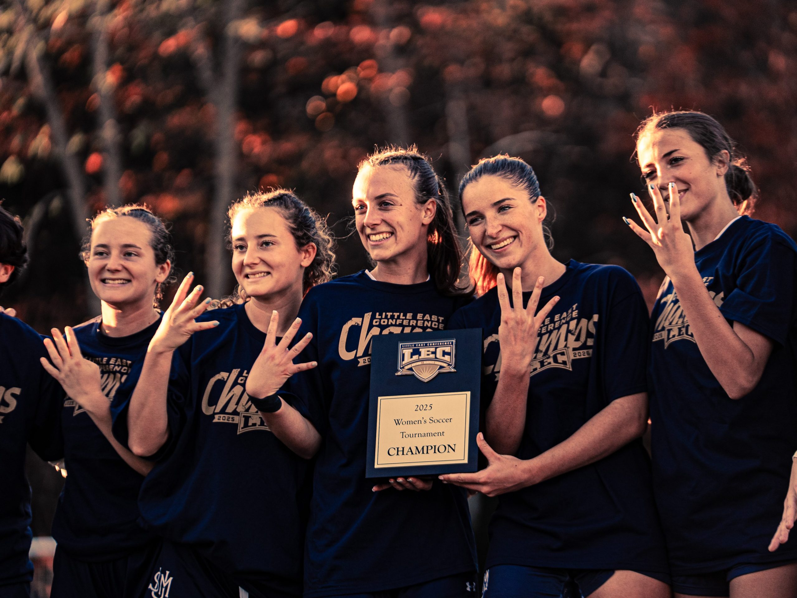 USM women’s soccer seniors smiling and holding up four fingers to celebrate their Little East Conference win.