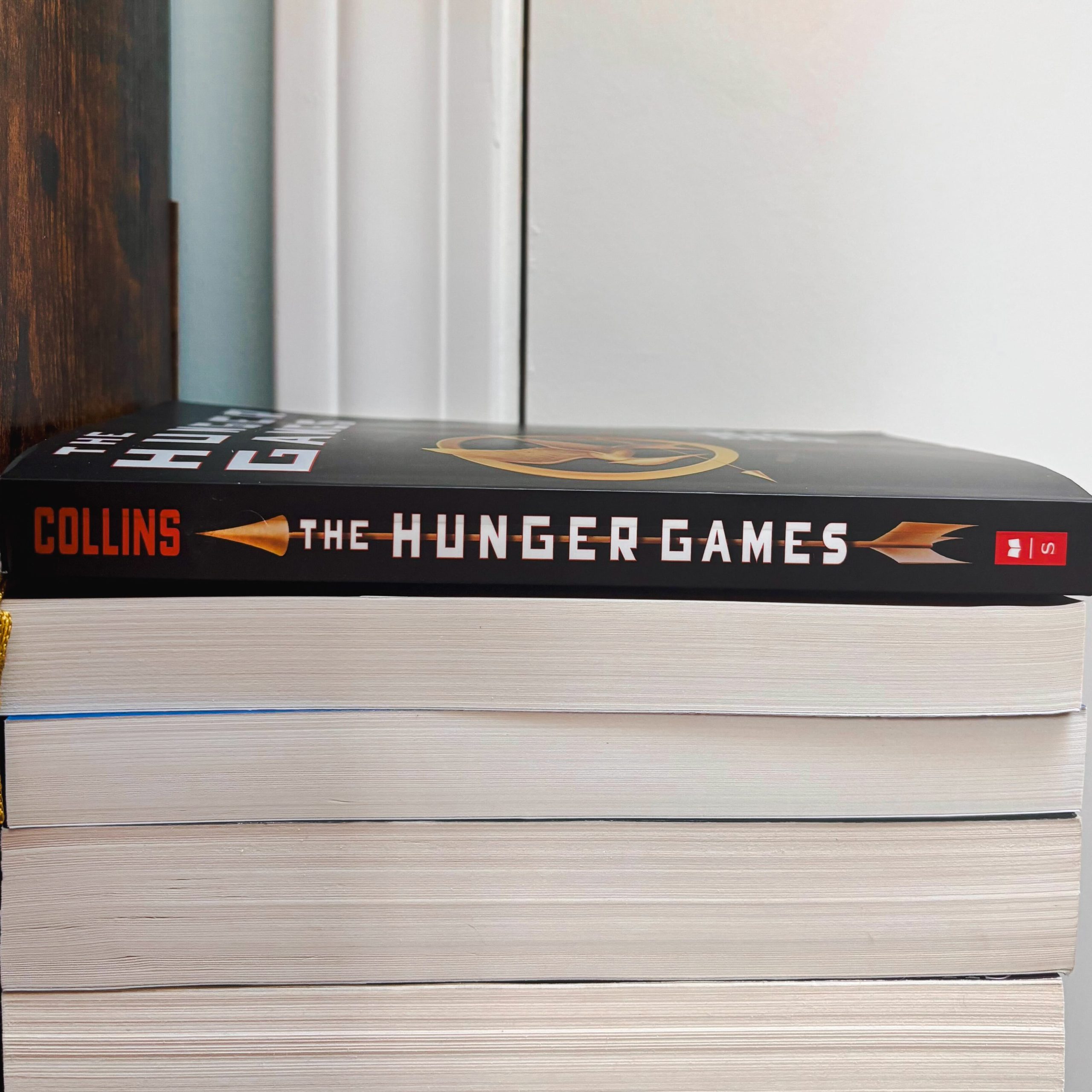 A pile of books viewed from the side, with page edges visible and The Hunger Games resting on top, spine facing outward.