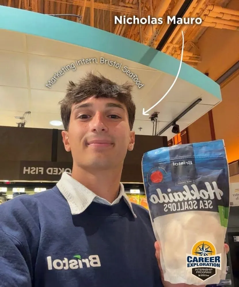 Nicholas Mauro holding a bag of frozen sea scallops while wearing his Bristol branded sweater.