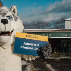 USM mascot Champ the Husky displays an Admitted Students Day sign on the Gorham campus