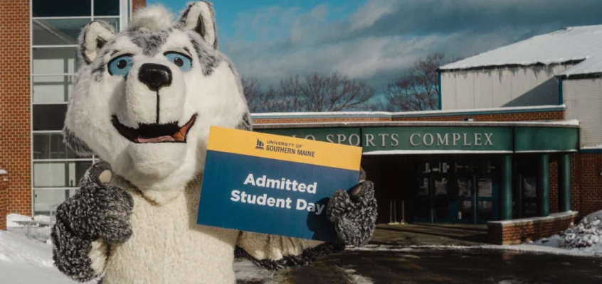 USM mascot Champ the Husky displays an Admitted Students Day sign on the Gorham campus
