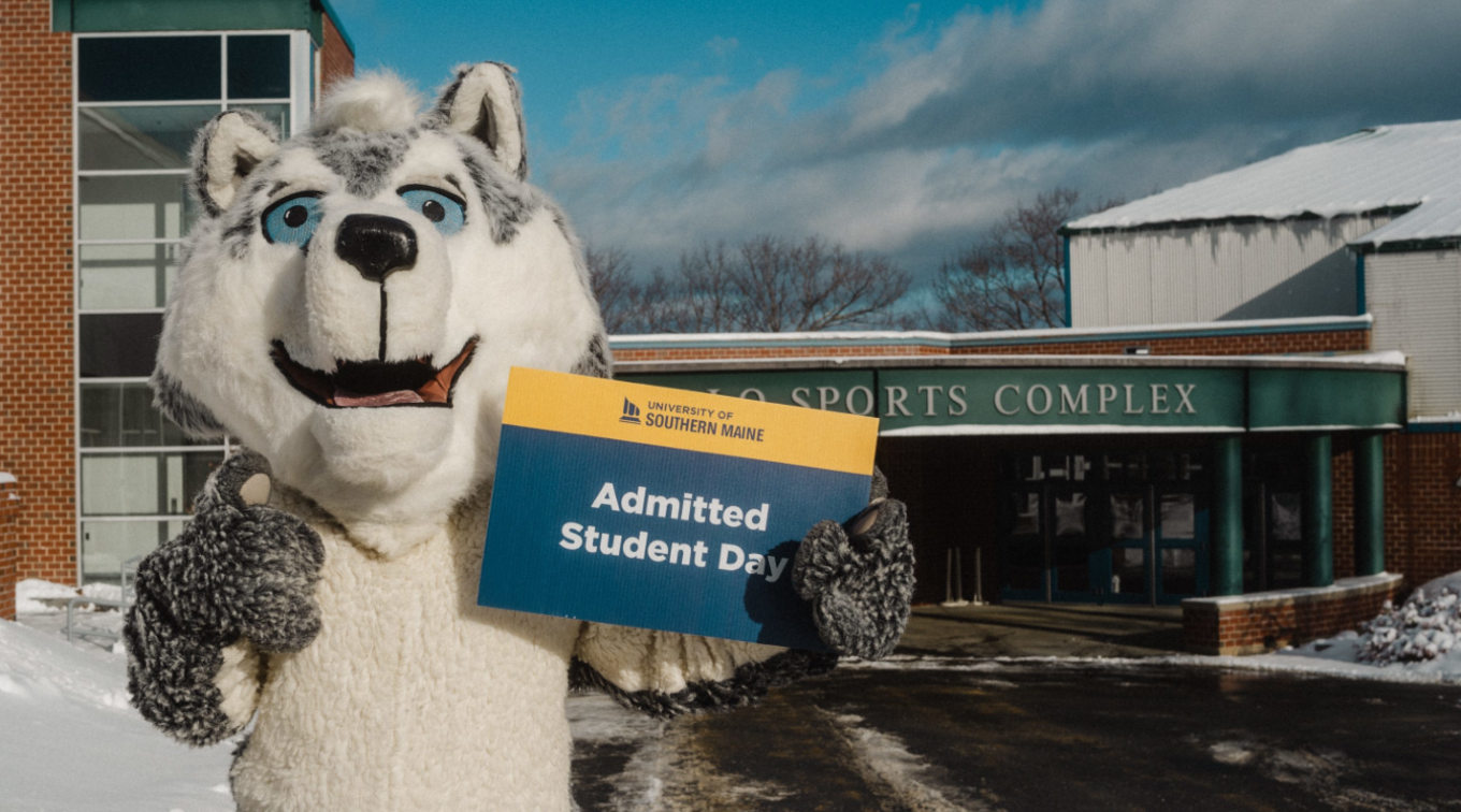 USM mascot Champ the Husky displays an Admitted Students Day sign on the Gorham campus